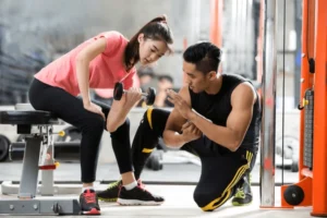 Personal trainer teaching fitness exercises to an Asian woman at the gym.